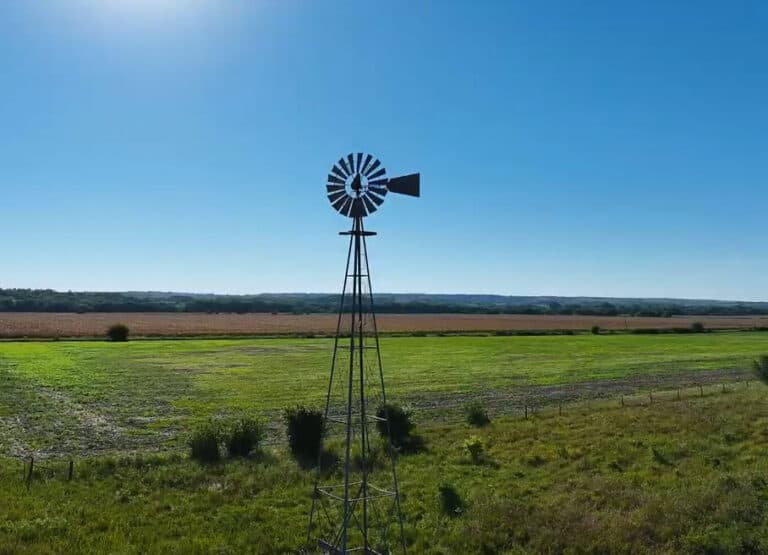 A windmill in the middle of a field with a blue sky.