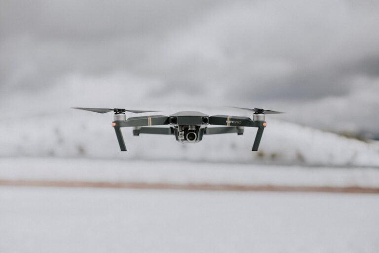 A black drone flying over a snowy field.