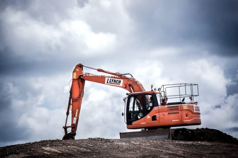 An orange excavator sits on top of a dirt hill.
