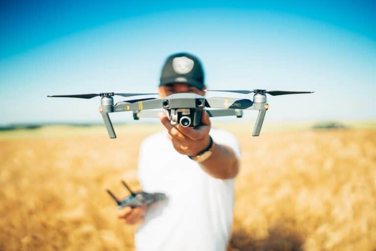 Person holding drone in field, remote control in background.